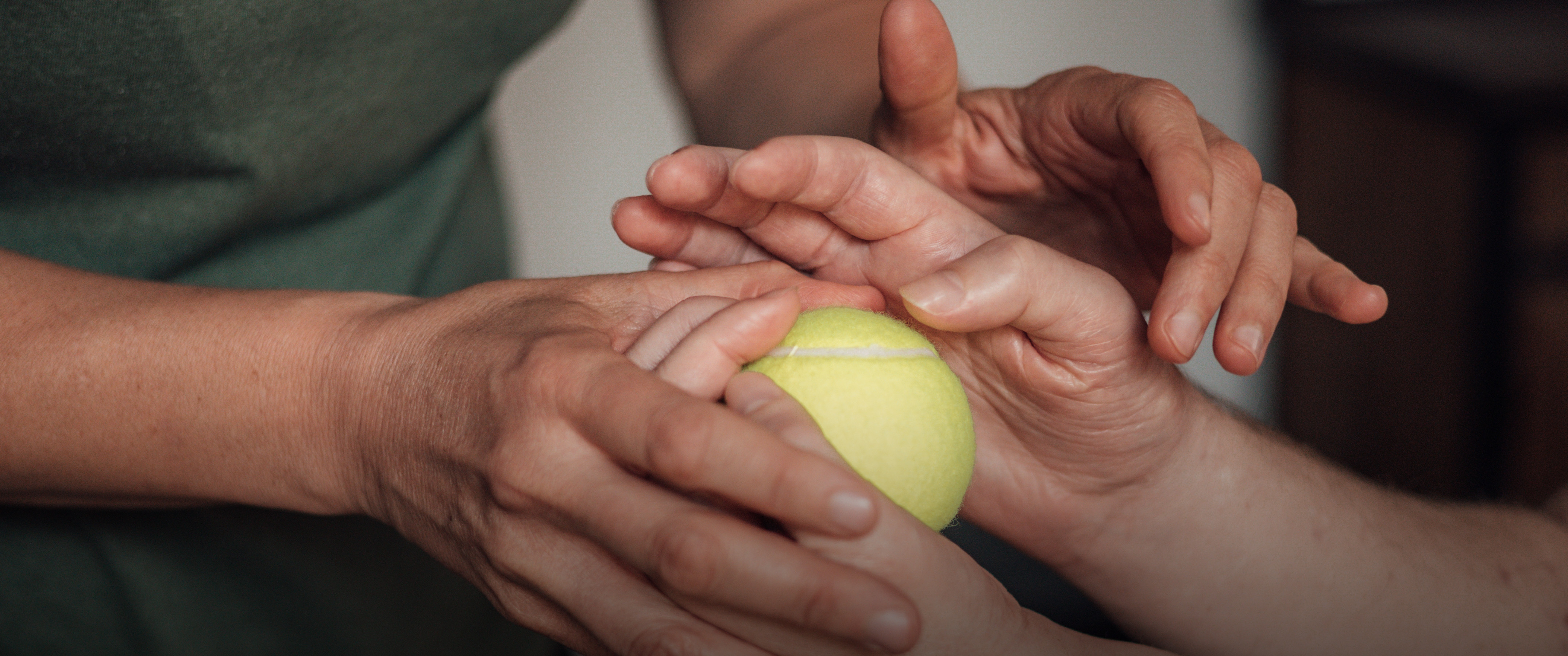 Luka Krizanac’s hands holding a tennis ball, while his physical therapist is holding his hands in hers