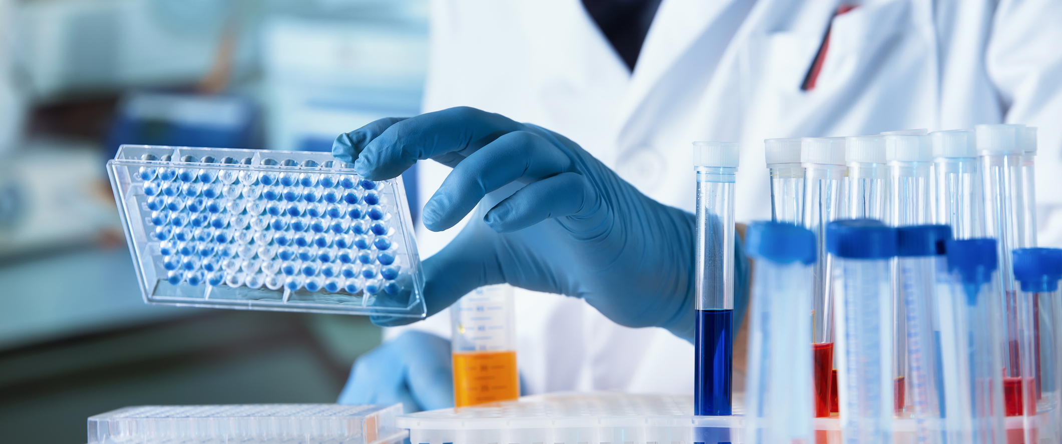 A doctor holding a microplate with test tubes on a table in a lab
