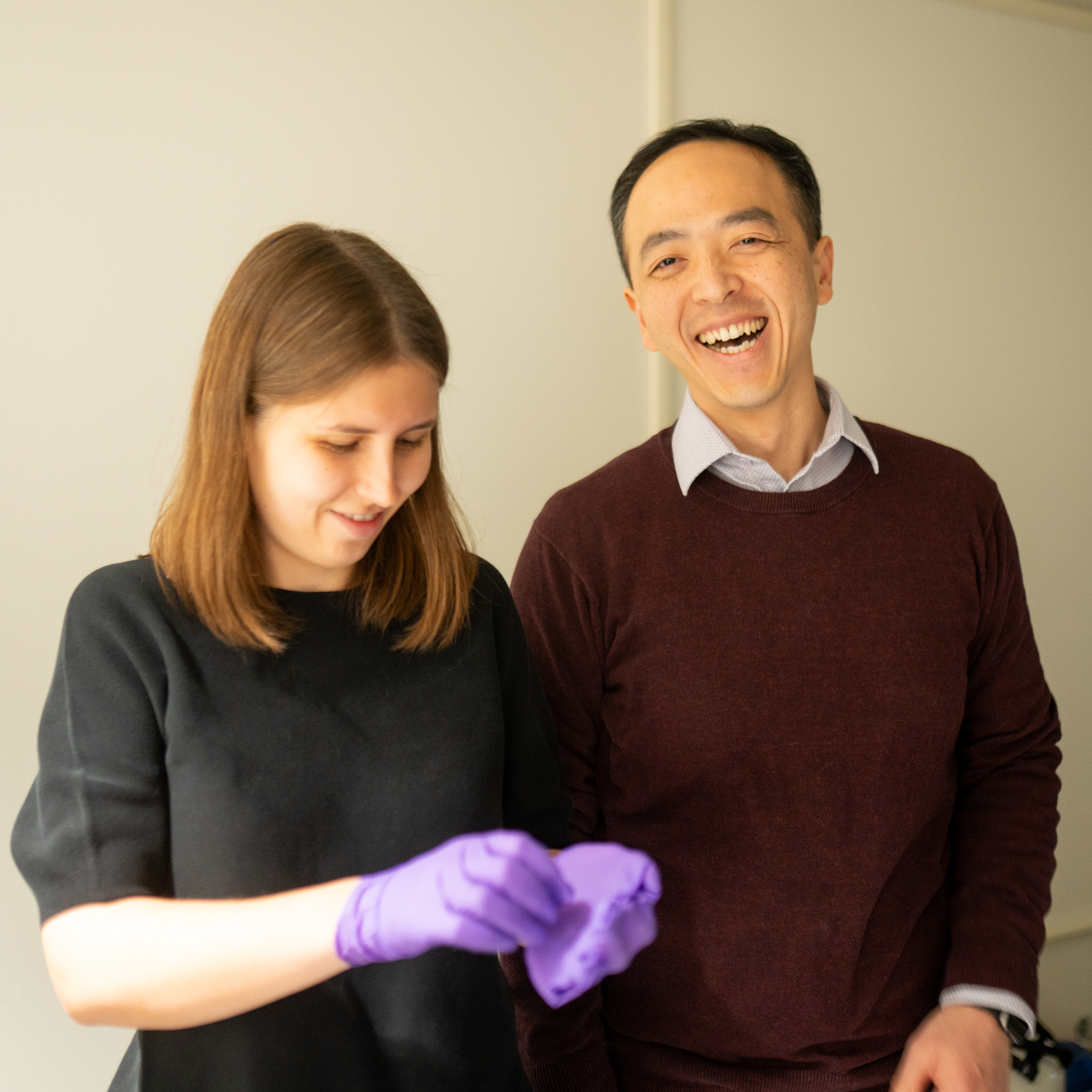 Kathryn Kixmoeller looks down at her hands in gloves, standing next to Yi-Wei Chang, who is smiling