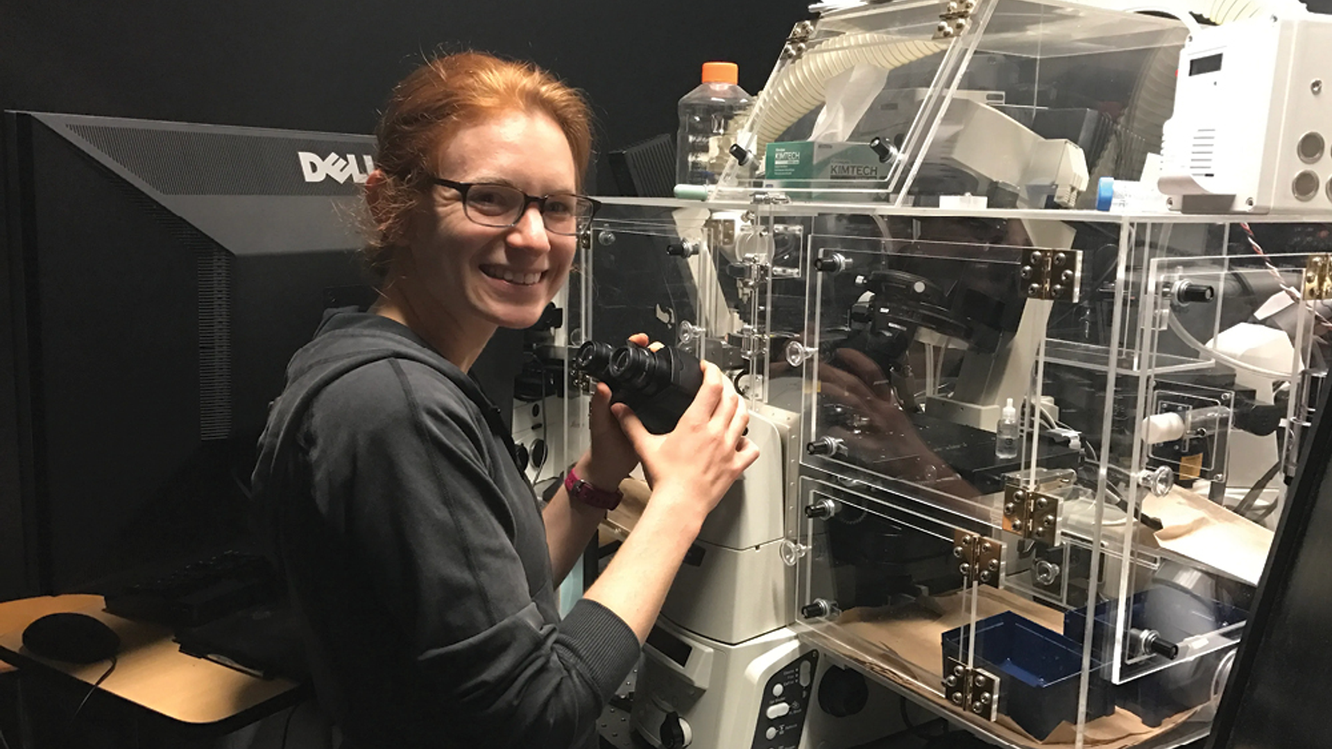 Portrait of Sydney Shaffer standing next to a large microscope in a medical lab