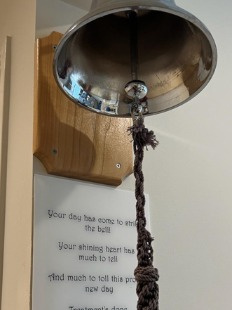 A close up of a silver cancer bell, with an inspirational poem about cancer on a placard under it.