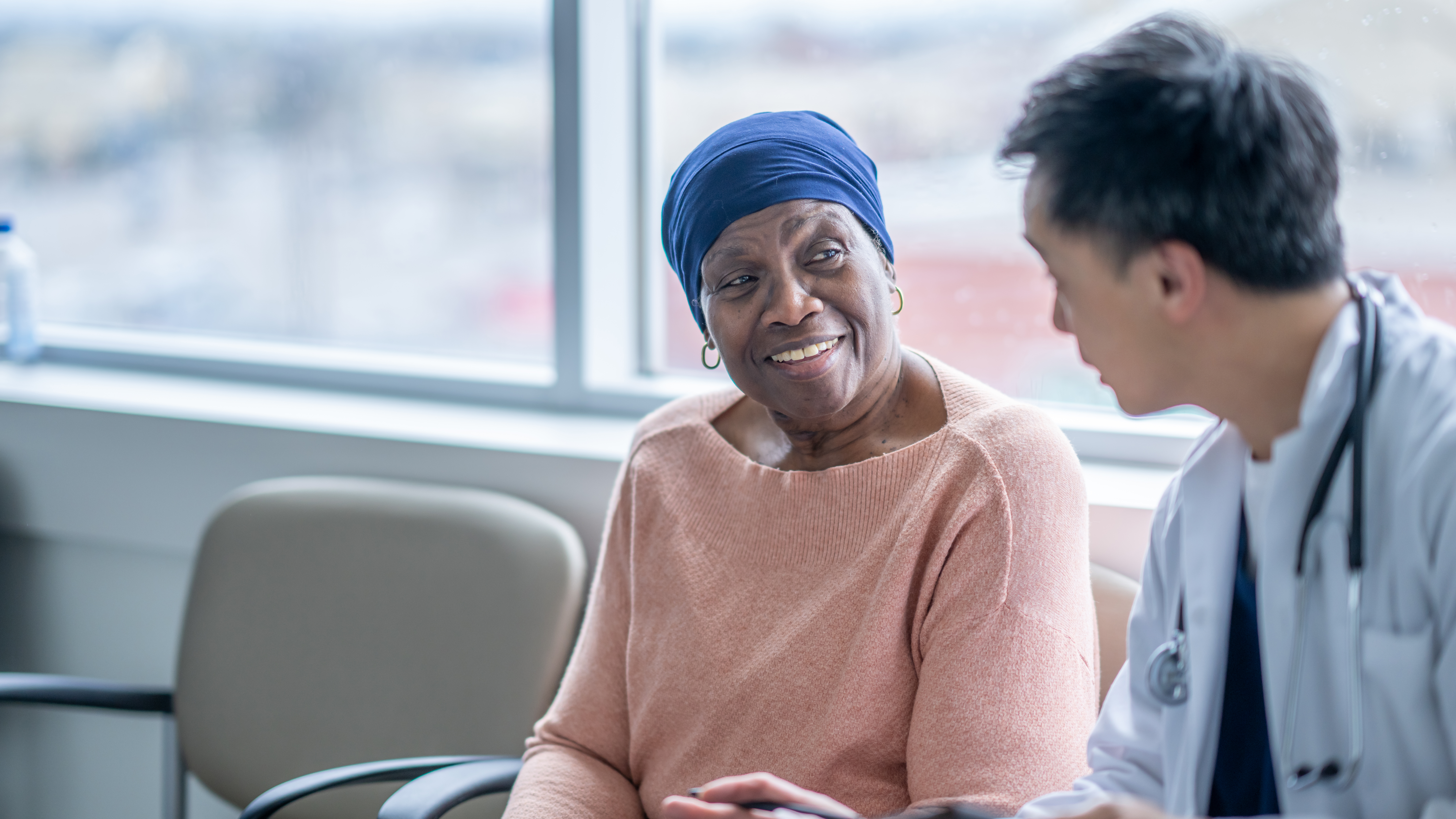 A senior cancer patient, sits in a waiting room with her doctor during a check-up