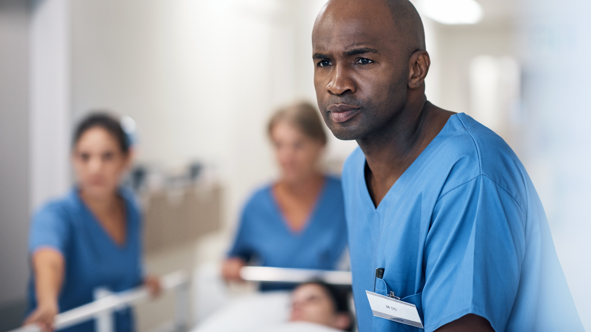 Cropped shot of a handsome mature male nurse and his team pushing a patient down the hallway in a gurney.