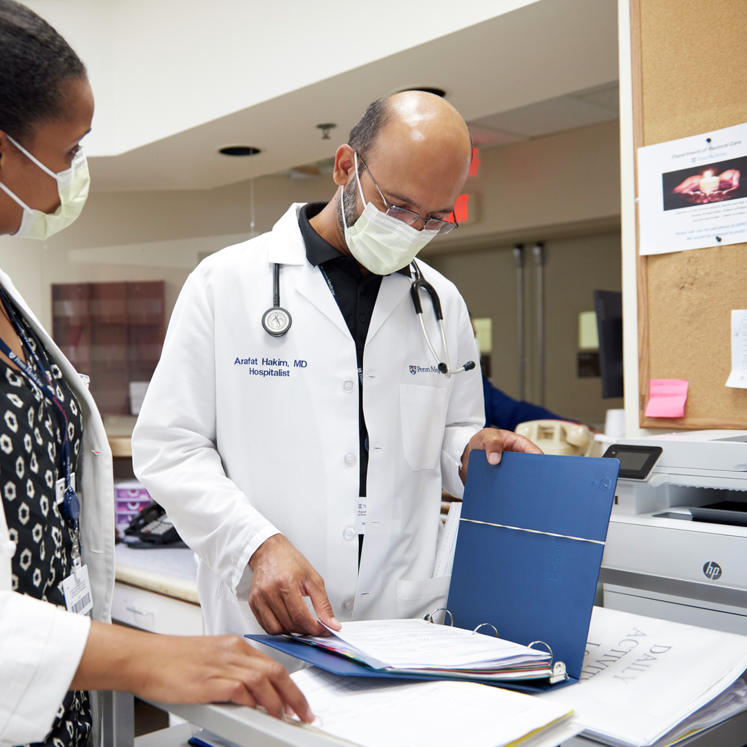 A female and male doctor in white coats look at a binder together