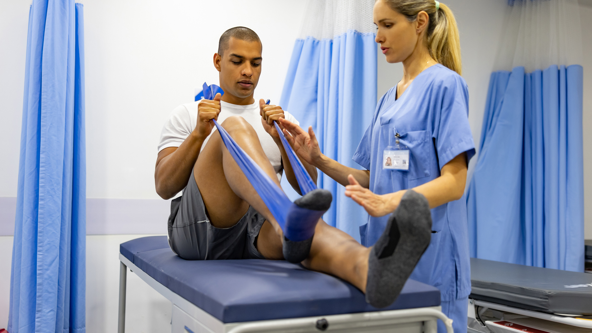 Male patient doing physical therapy exercises with the guidance of his therapist and using a resistance band.