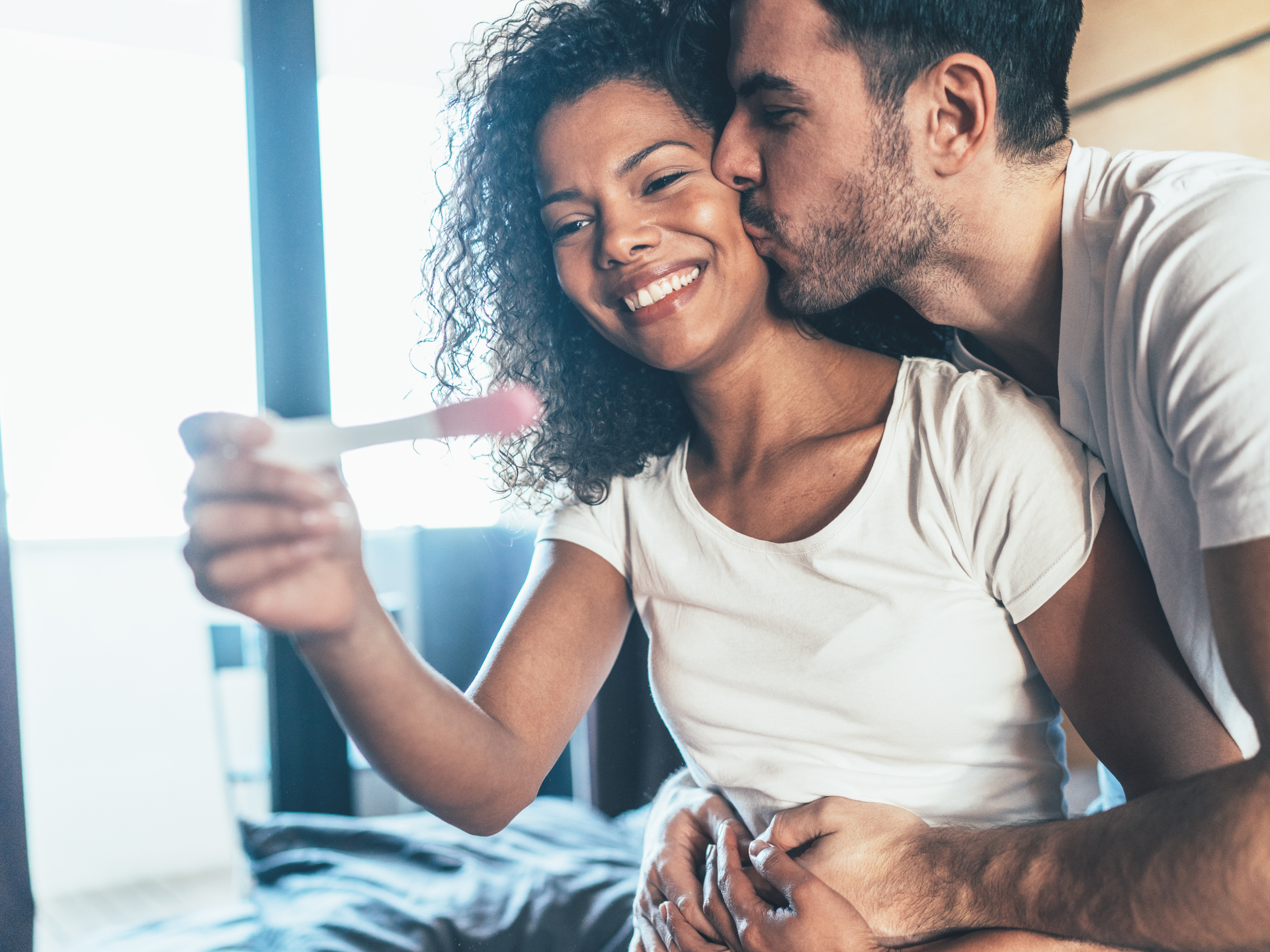 Happy couple with positive pregnancy test in the bed at home