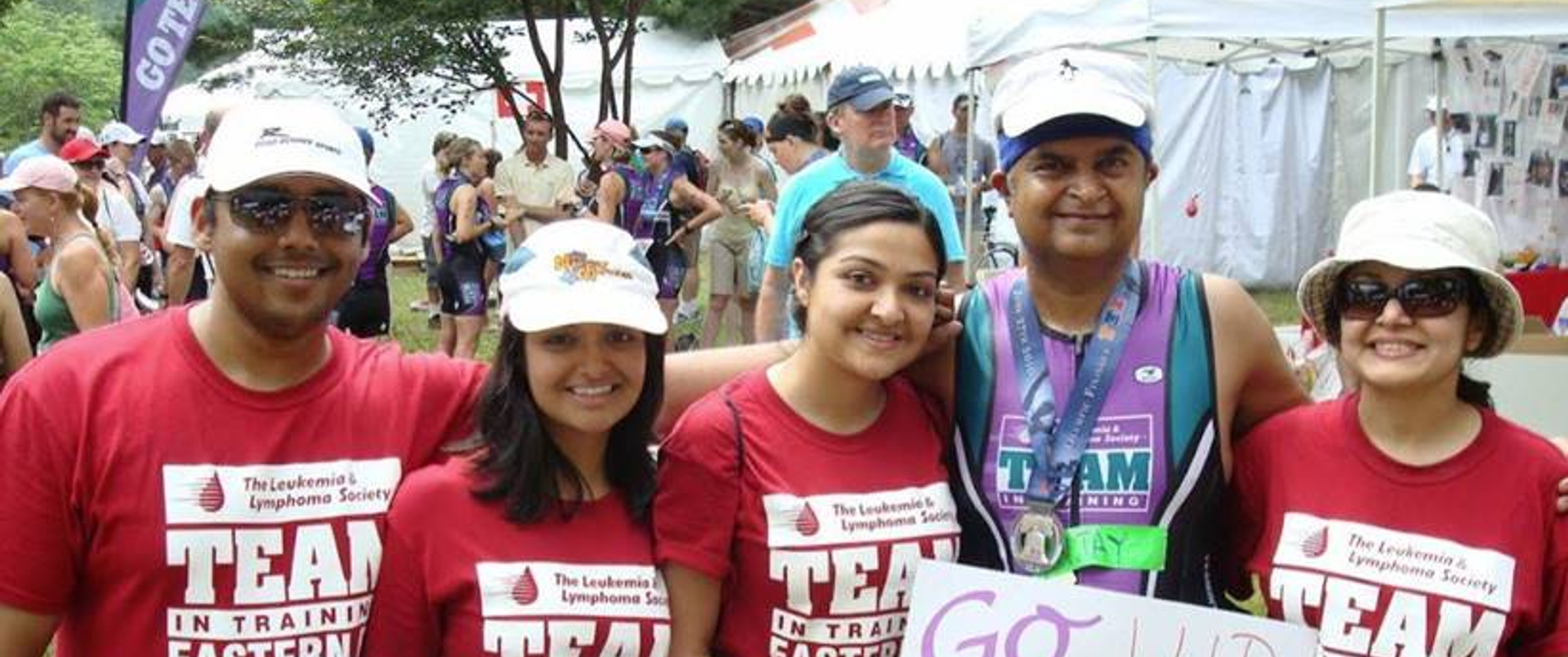 Sanjay Shah dressed in running gear with a group of family members in matching red T-shirts holding signs with supportive messages like "Go Sanjay"