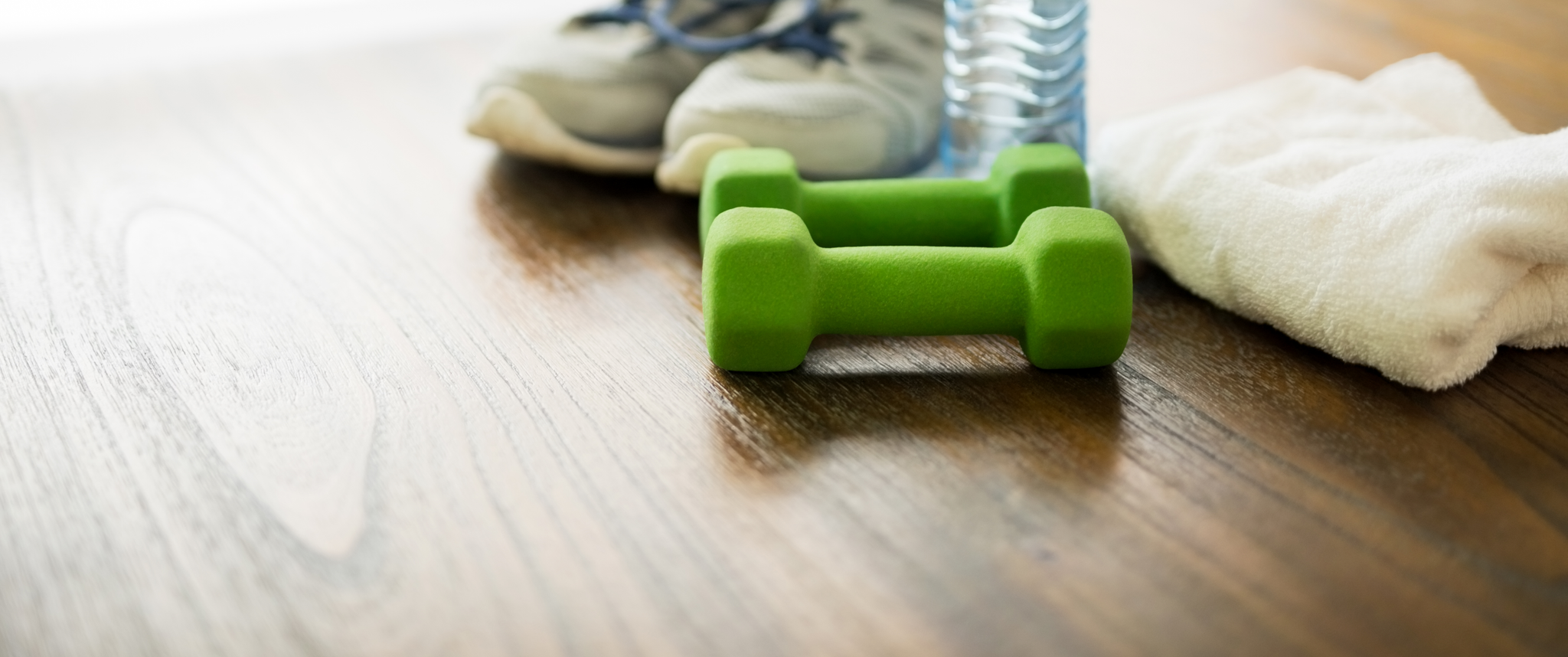 Dumbbells, sneakers, bottle of water and towel on wooden table
