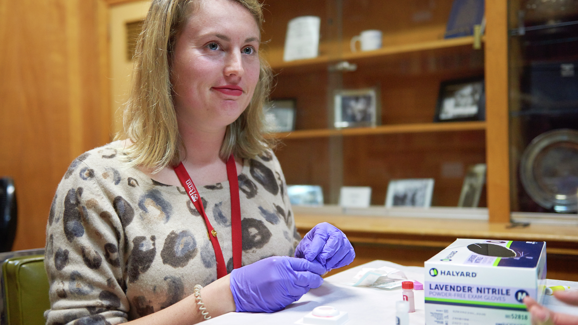 Meredith "Page" Miller, a young woman wearing latex gloves, has a serene expression
