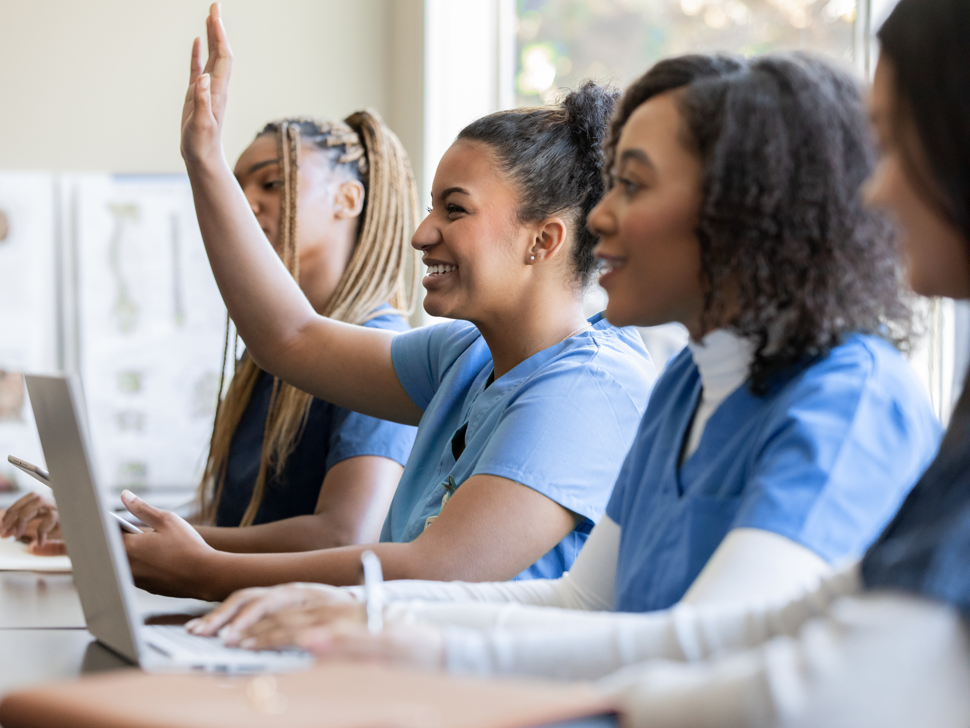 young woman raises hand to answer question during class with other nursing or medical students