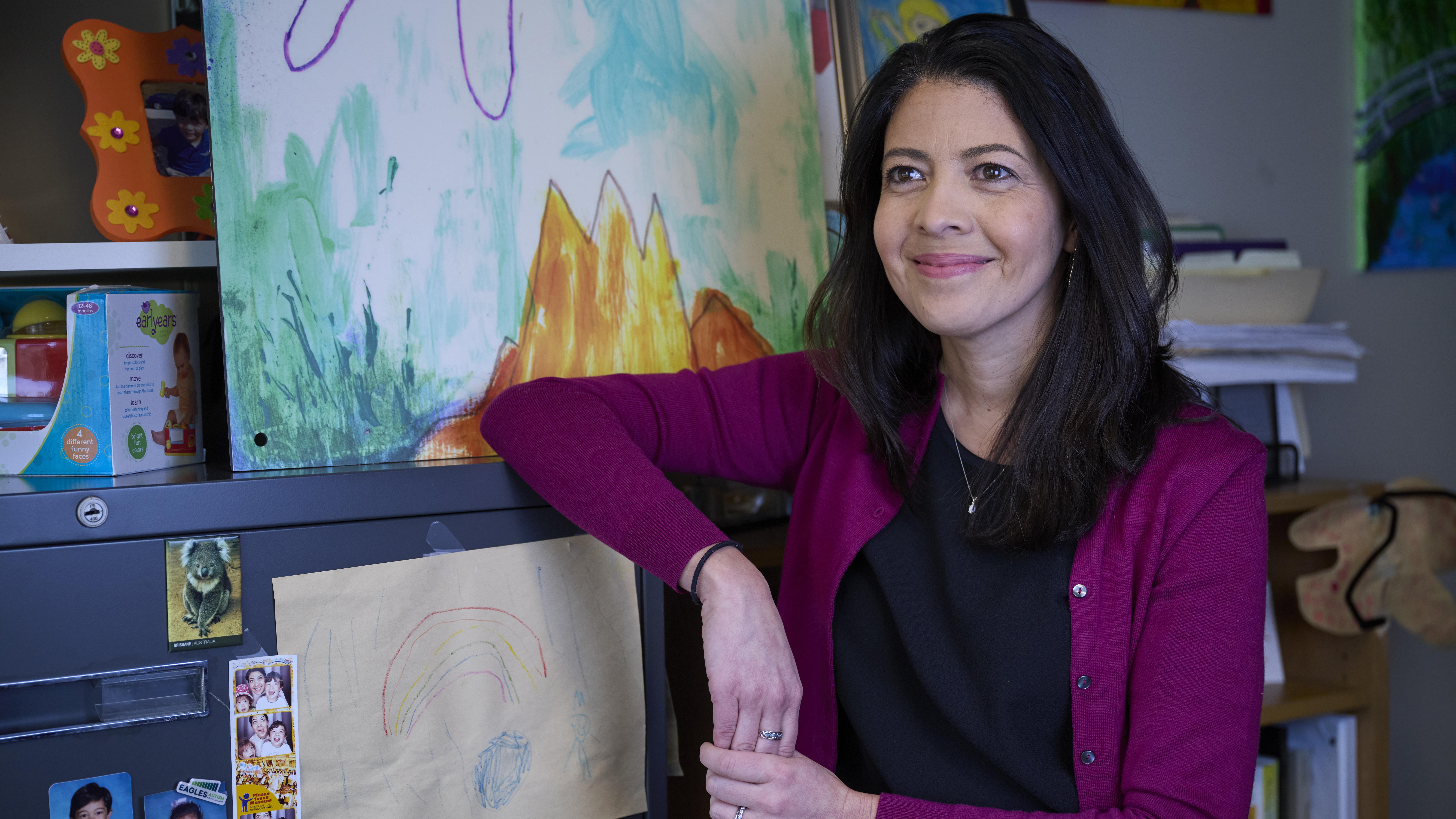 Melanie Pellecchia, standing next to a file cabinet, surrounded by children's artwork and photos