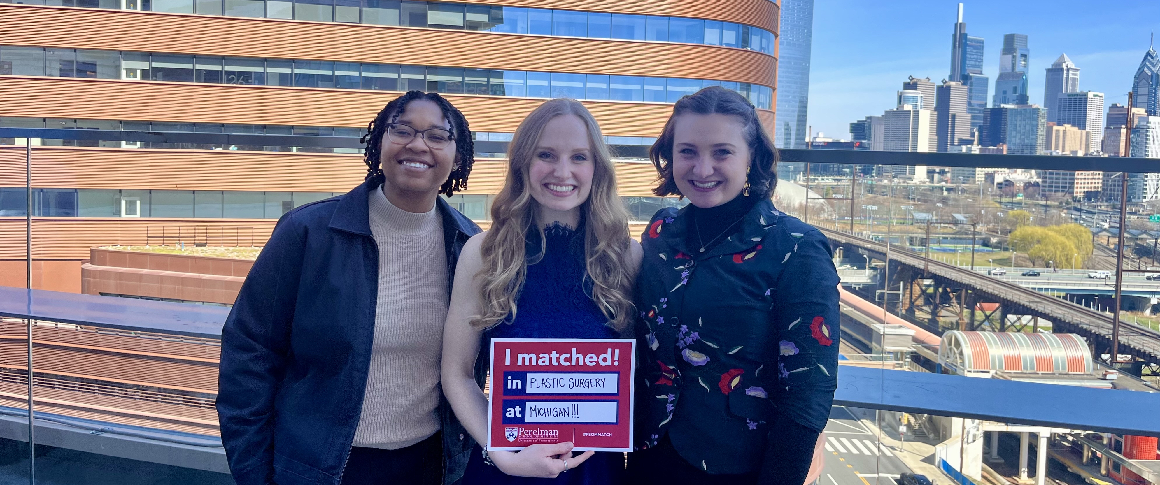 Holly Cordray holding a Match Day poster and standing with two friends outside, with the Clifton Center in the background