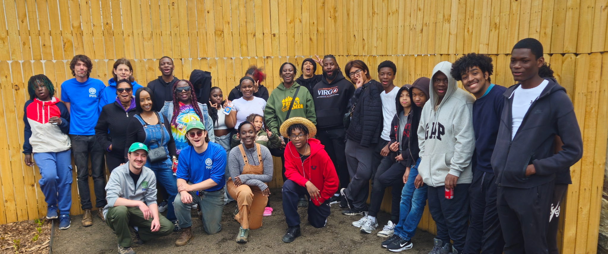 A group of people in gardening clothes in front of a large wooden fence