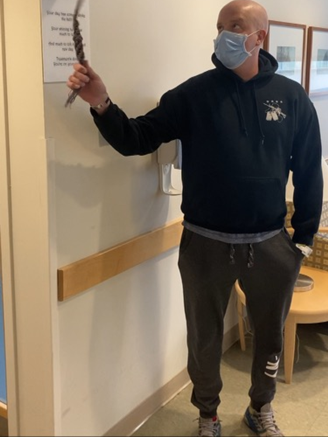 Chris Naimo, wearing a mask, rings a cancer bell