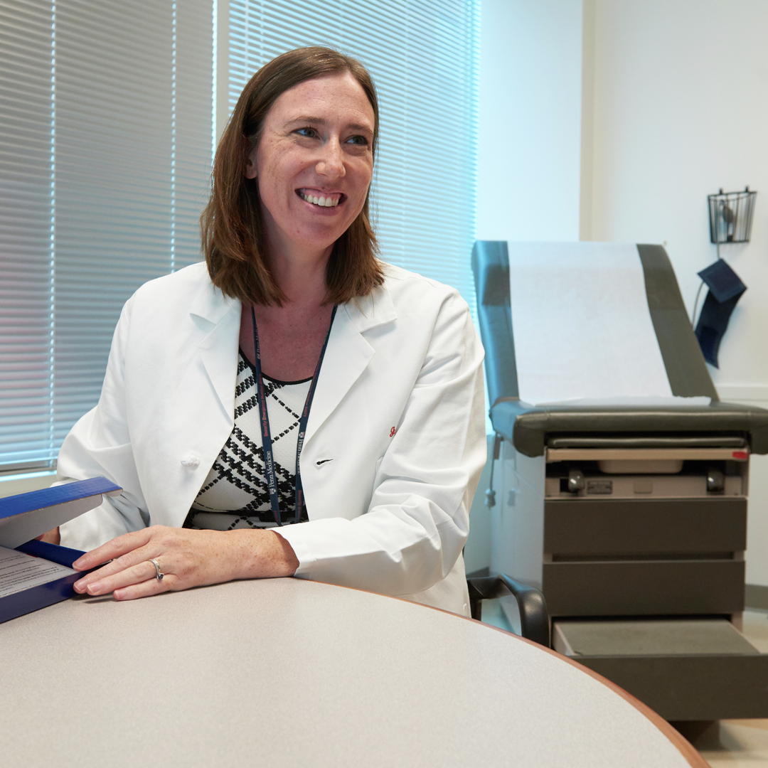 Corinne Rhodes, MD, smiles in an exam room while opening a box containing a FIT kit