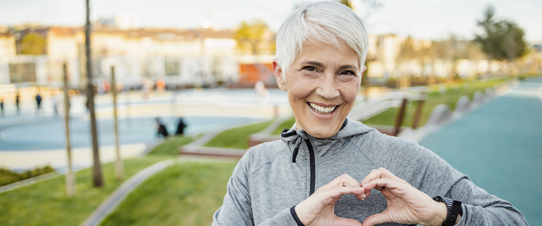 Portrait of smiling senior woman with short hair in sports clothing making a heart sign with her hands