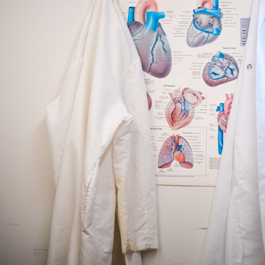 A white lab coat hangs on a wall next to a poster of the anatomy of the heart
