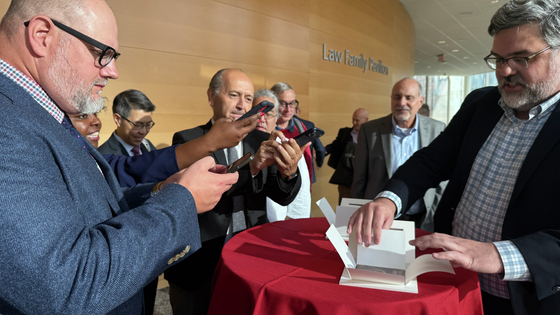 Penn Archivist John Bence standing at a small table pulling back the cardboard casing of one of Arthur Goodspeed’s X-ray plates, as Perelman School of Medicine leaders snap photos