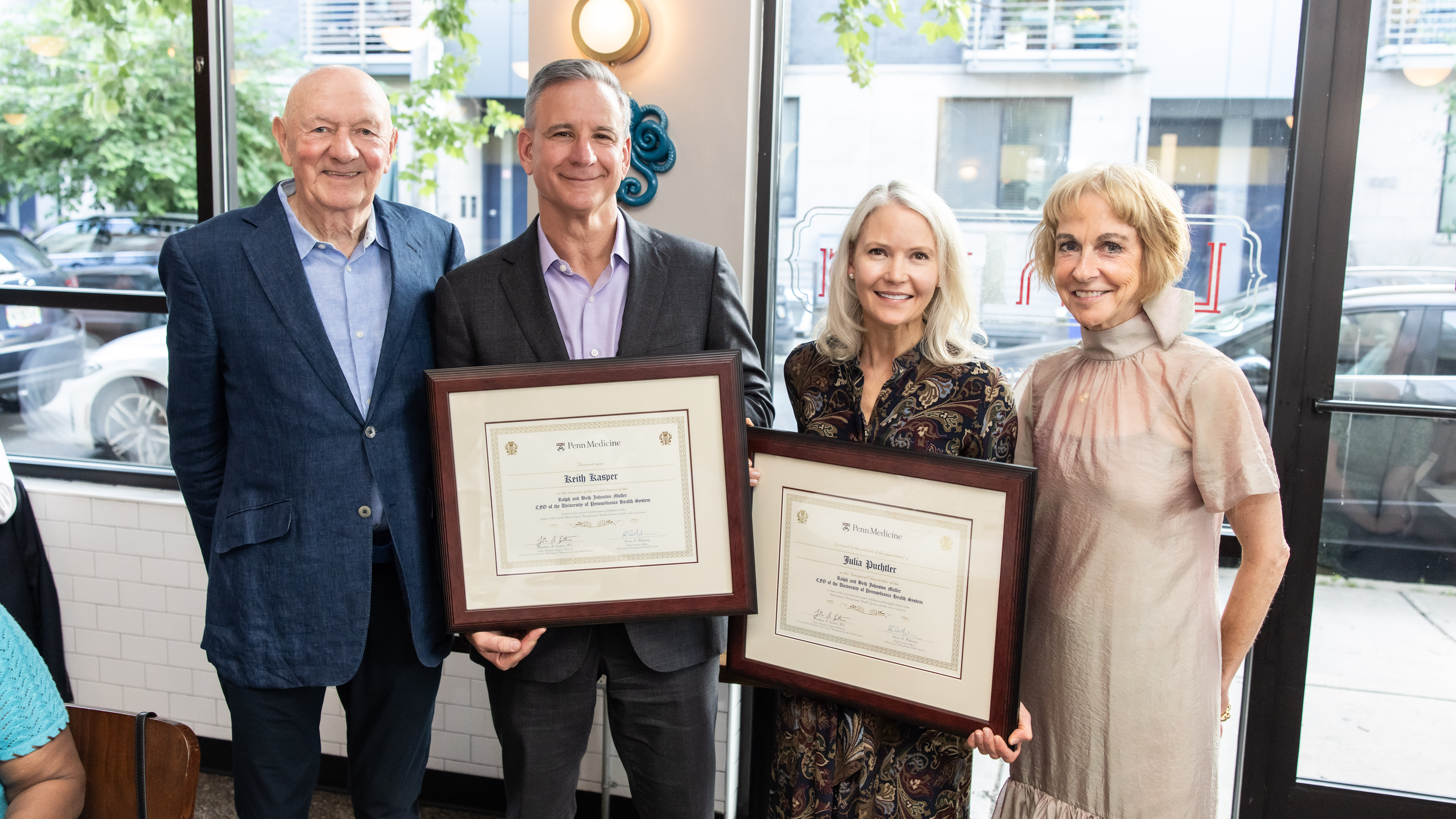 Keith Kasper and Julia Puchtler hold framed certificates recognizing them, with Ralph Muller and Beth Johnston Muller standing on either side