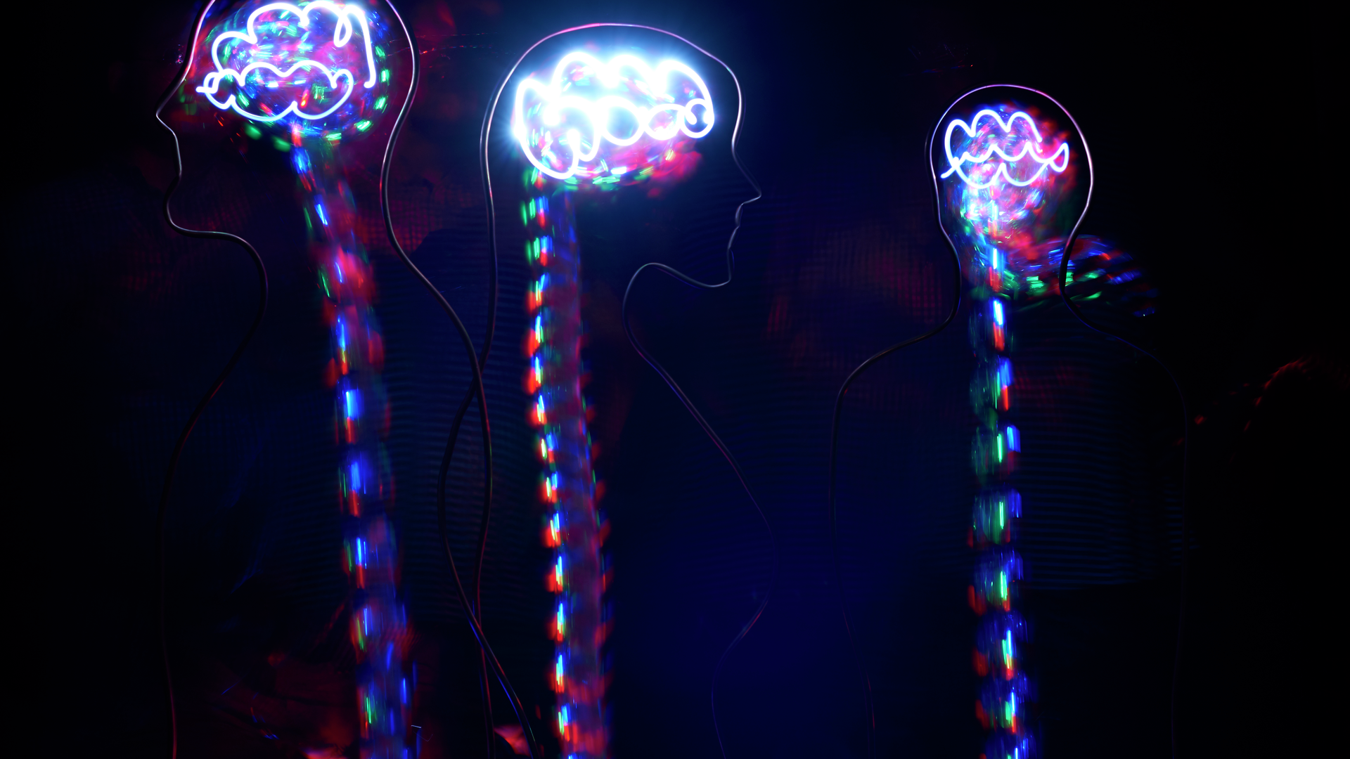 Three wire silhouettes in the darkness are filled with brain and spine shapes made up of colorful light