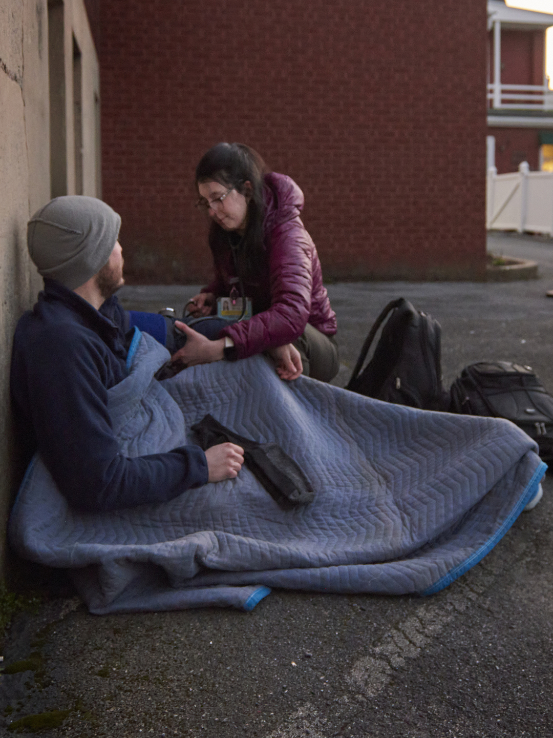 Samantha Bush, DO, takes a blood pressure reading from a man lying under a blanket in a parking lot