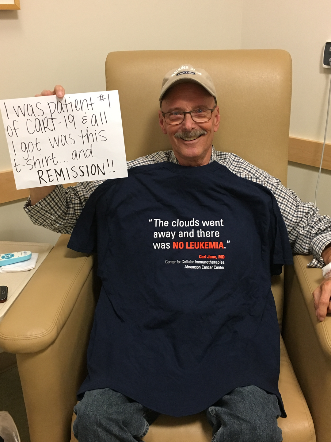 Bill Ludwig holds sign saying I was patient #1 of CART-19 & all I got was this lousy T-shirt...and remission! Wearing a shirt with a Carl June quote