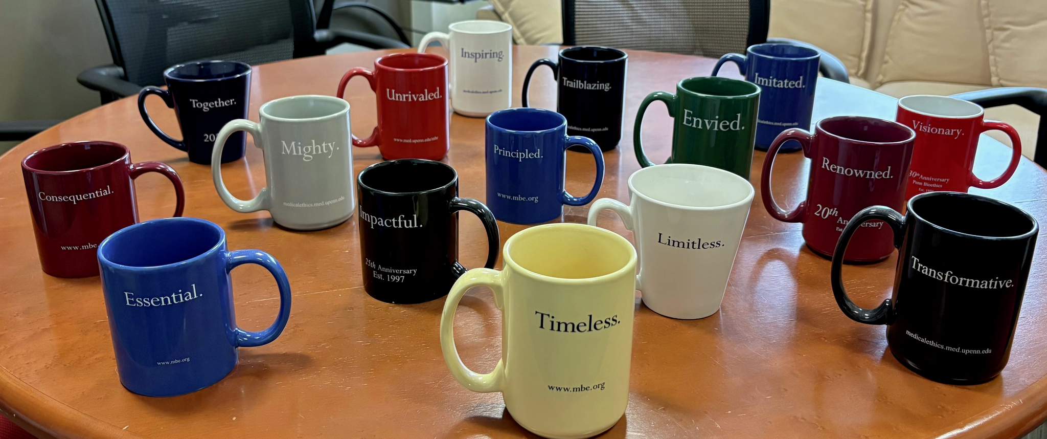 Colorful coffee mugs on a round table, each printed with words like Essential, Timeless, and Trailblazing