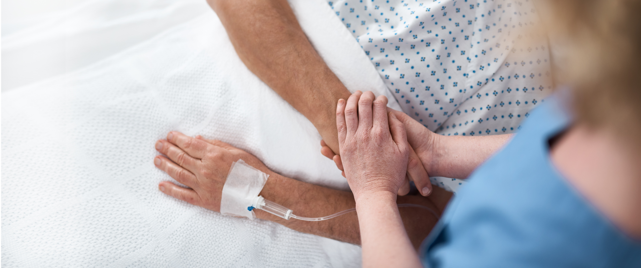 Female nurse holding hand of man in hospital bed 