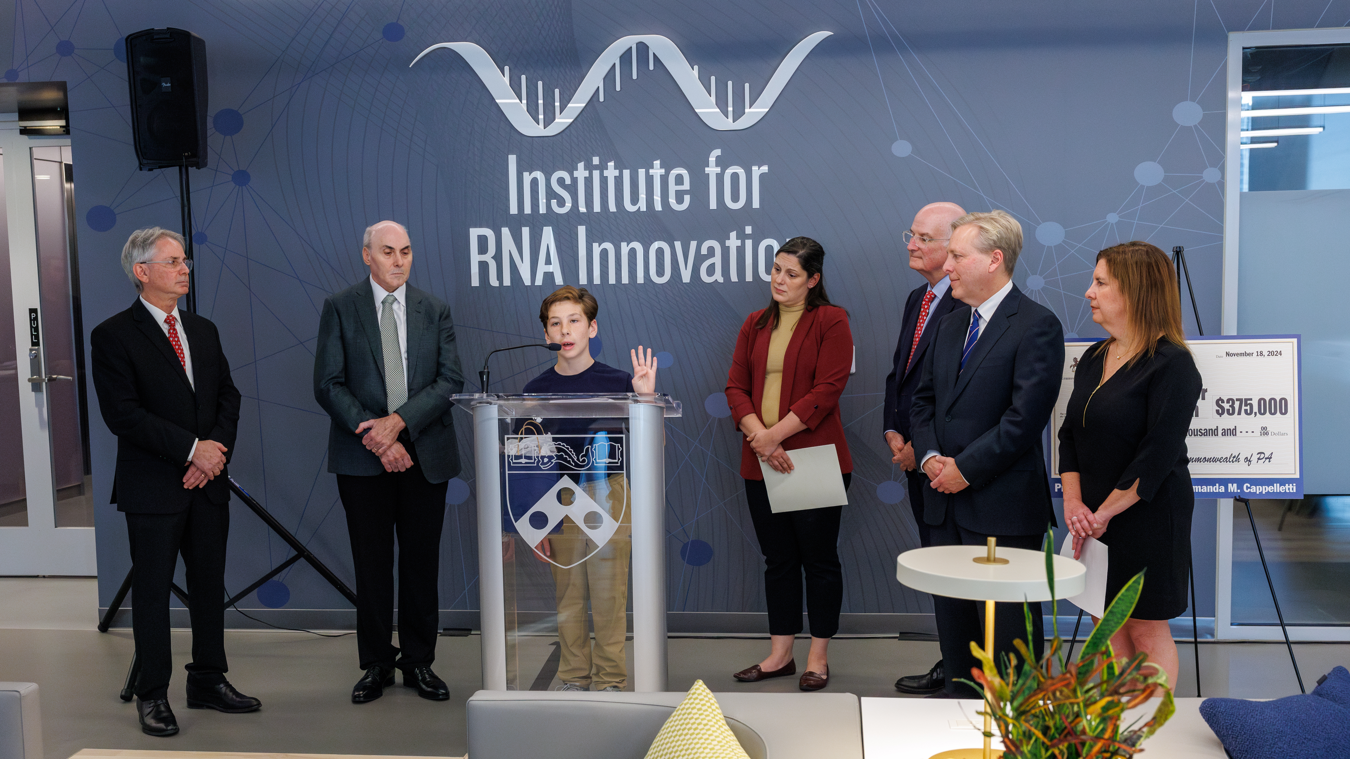 Jax Bari speaks behind a podium at the Penn Institute for mRNA Innovation