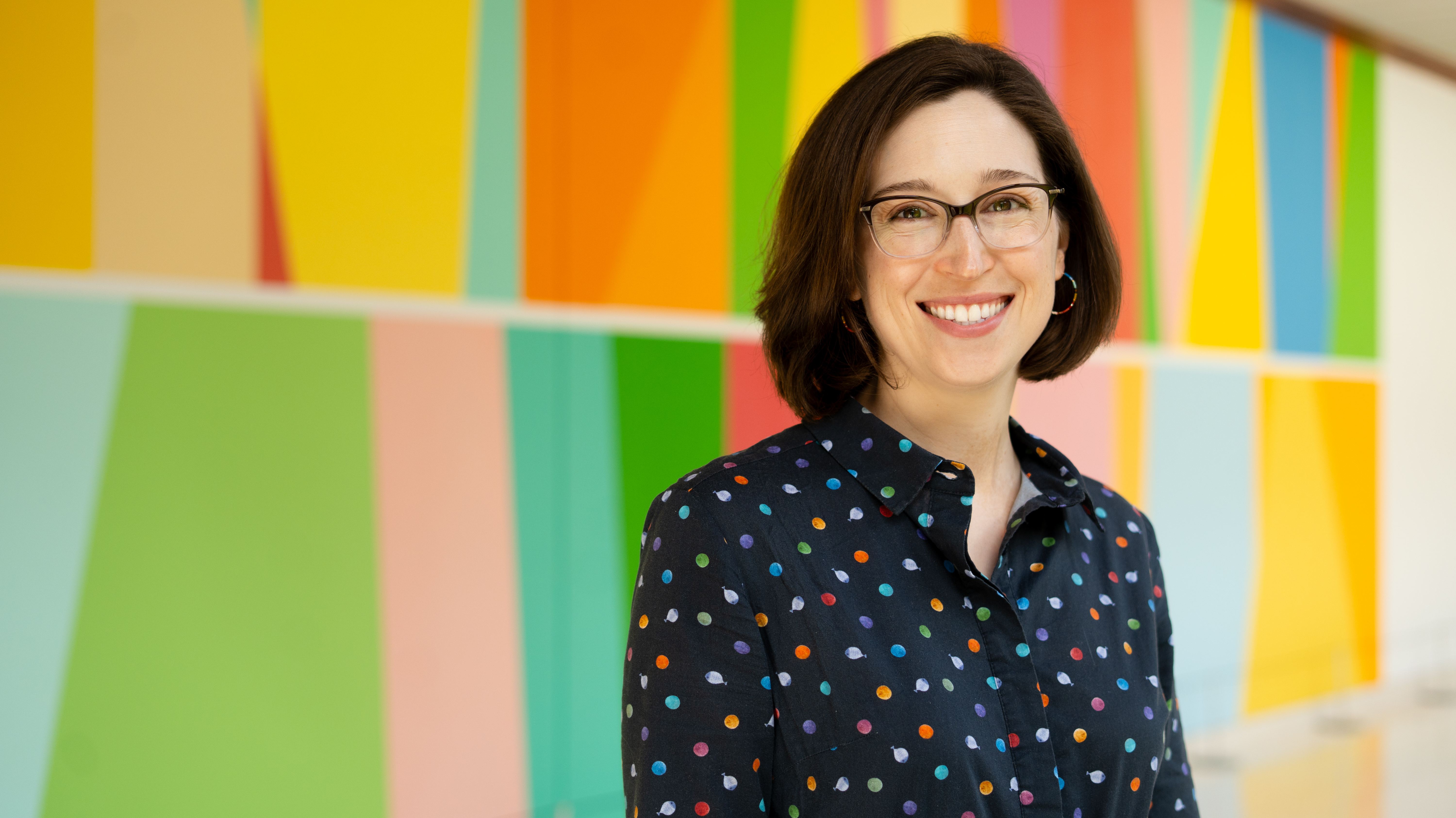 Katie Dalke smiling, in front of a multi-colored mural