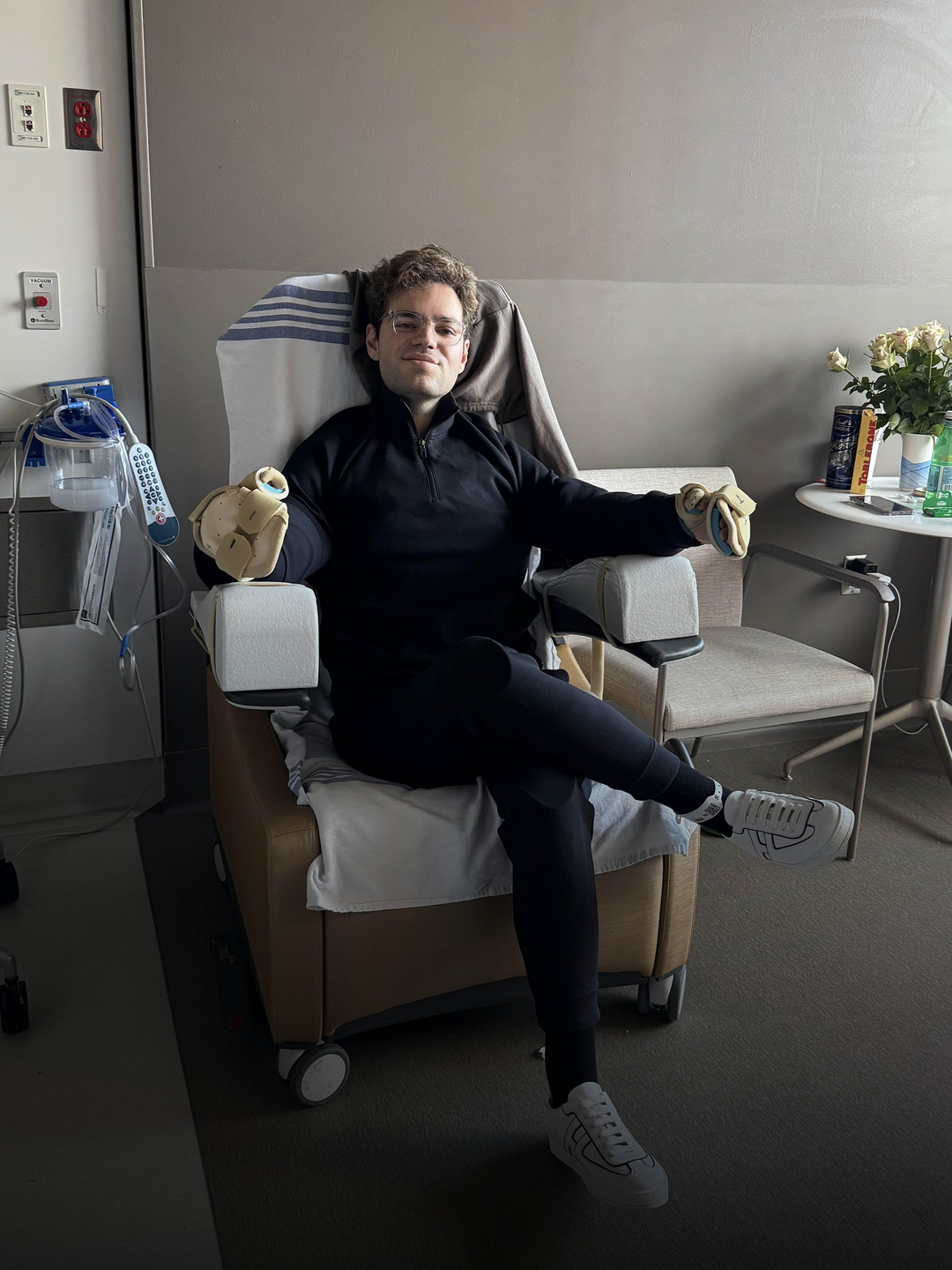 Luka Krizanac sitting in a chair in his patient room with casts on his hands and text of a photo courtesy in corner
