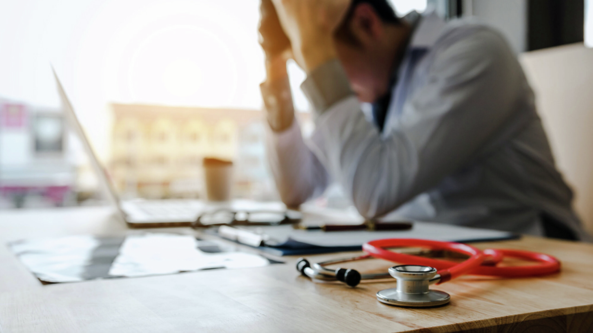 Physician holds his head in hands at desk