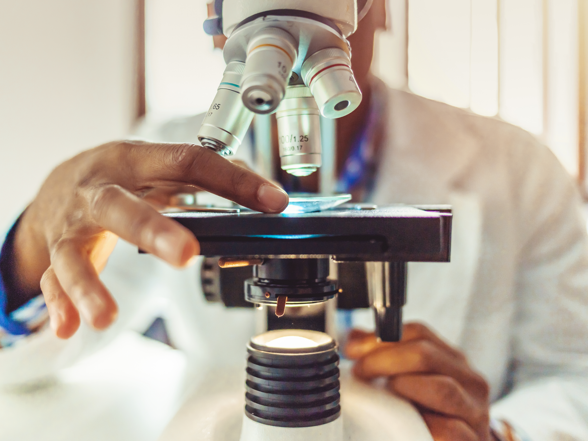 Male researcher at laboratory microscope with microscope slide in hand.
