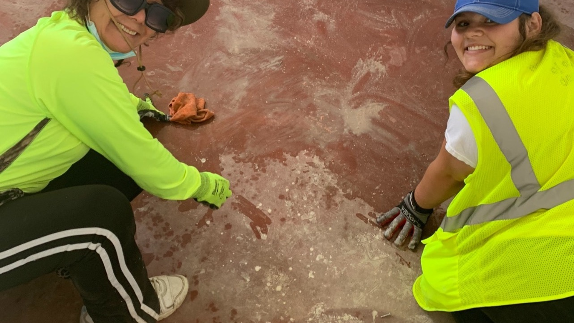 Maria Del Carpio and a teenage girl, both dressed in fluorescent yellow, kneel on a red clay floor and smile