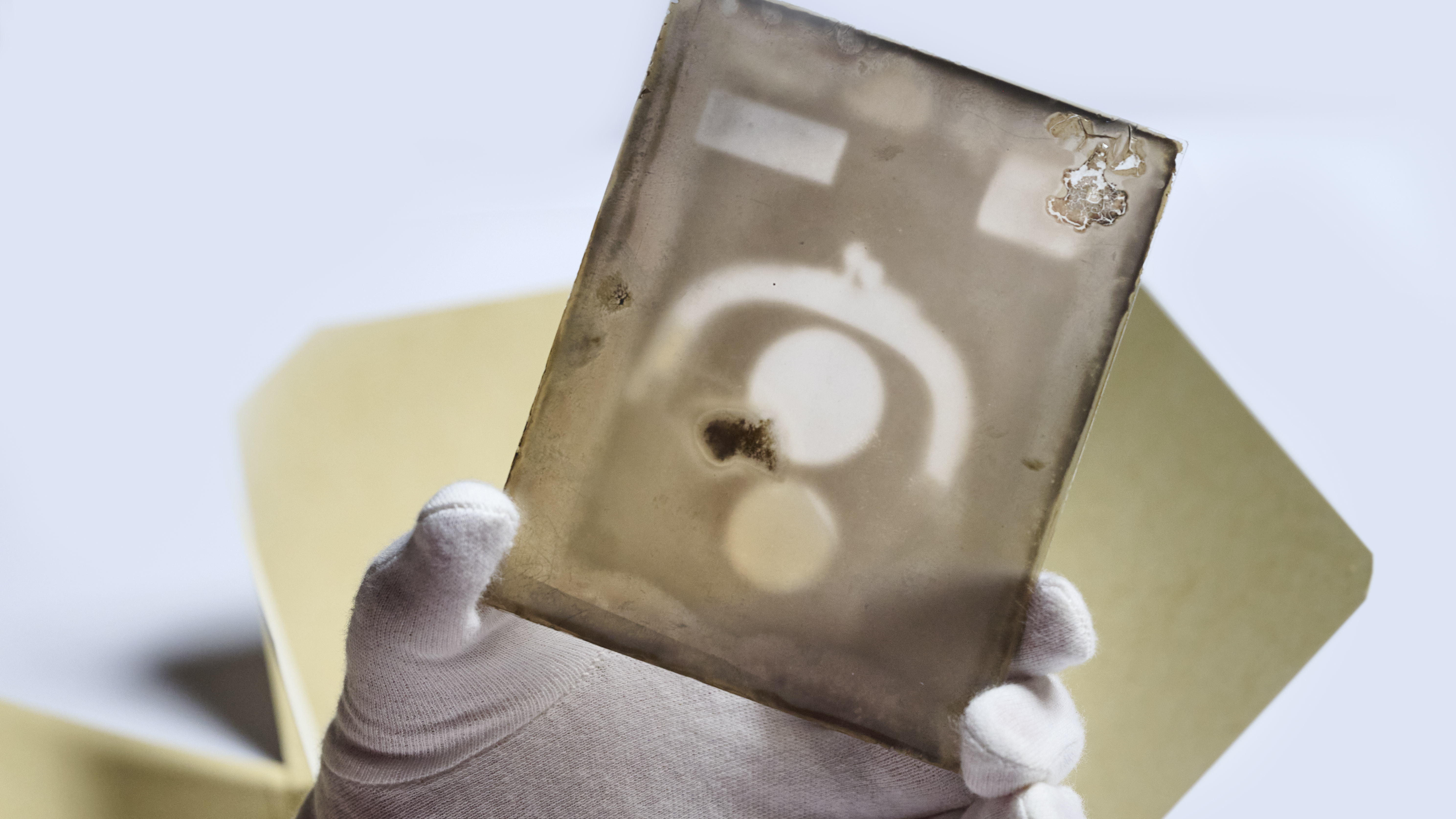 A gloved hand holding up a glass plate showing the outline of a coin purse and two circles inside