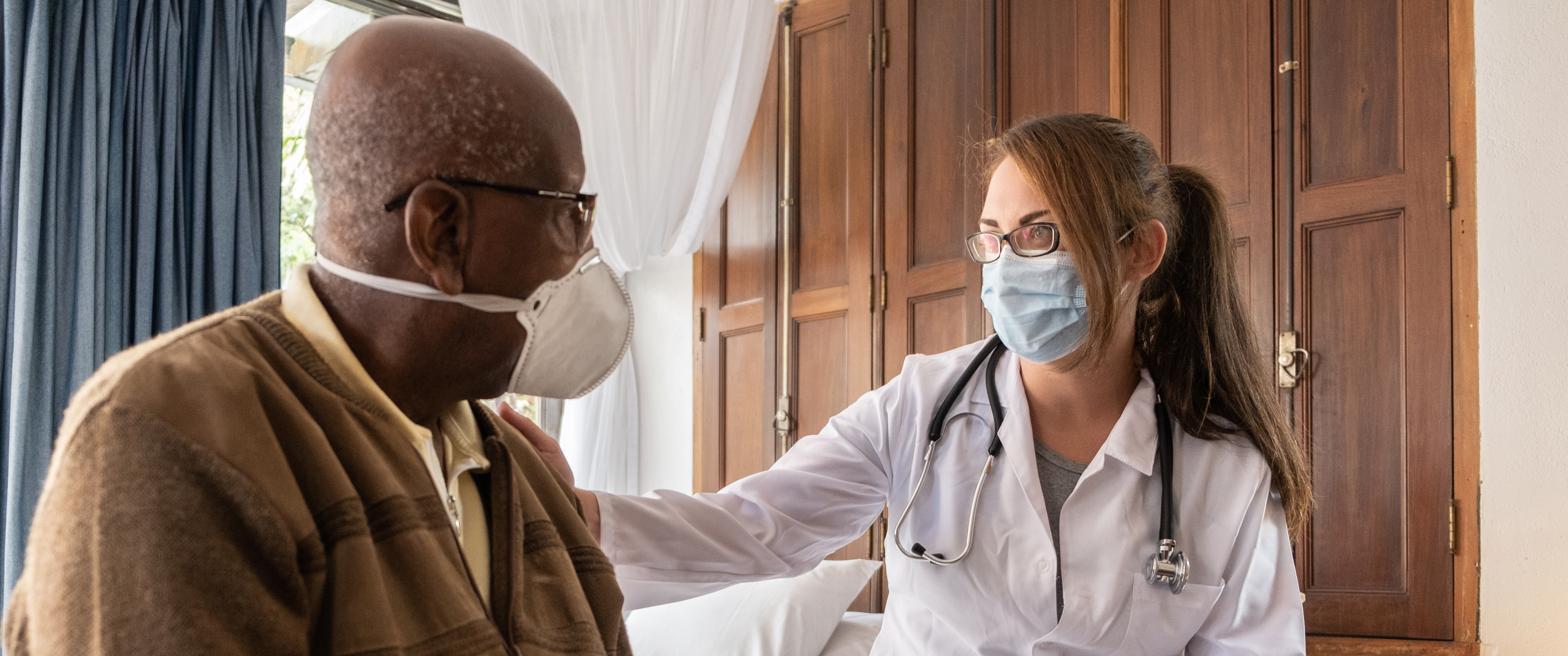 A doctor talks to an older patient while wearing masks