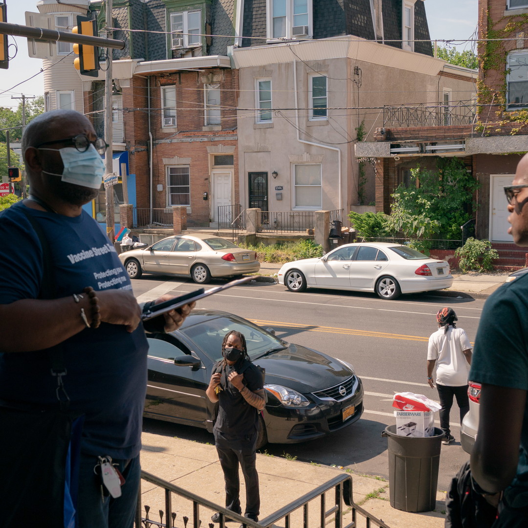 Several people look up from a Philadelphia street as Yuhnis Syndor speaks with a young man on a front porch