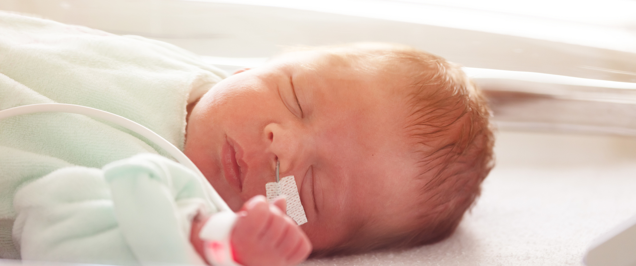 Close portrait of premature child with feeding milk through nose in ICU in hospital