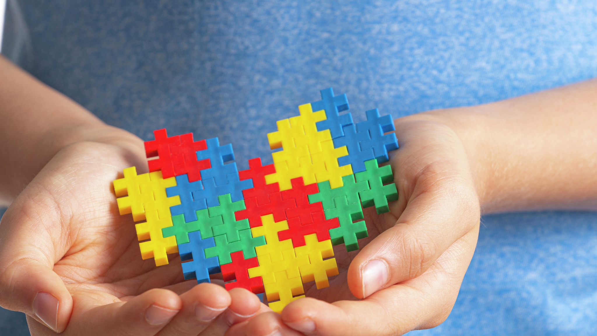 A child’s hands holding a colorful puzzle shaped like a heart