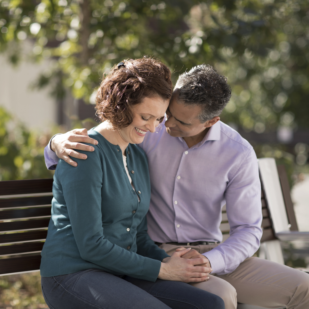 A cancer patient and their spouse embrace happily on a bench