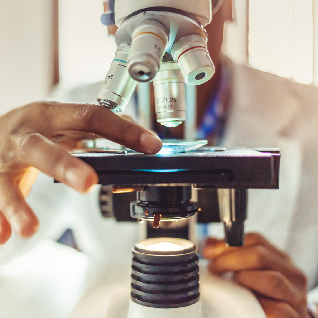 Male researcher at laboratory microscope with microscope slide in hand.