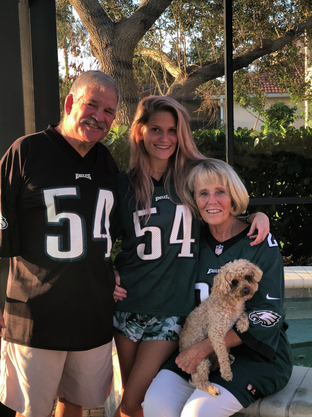 Kate Korson, a young woman with long flowing hair, poses with her parents, all wearing Eagles jerseys 
