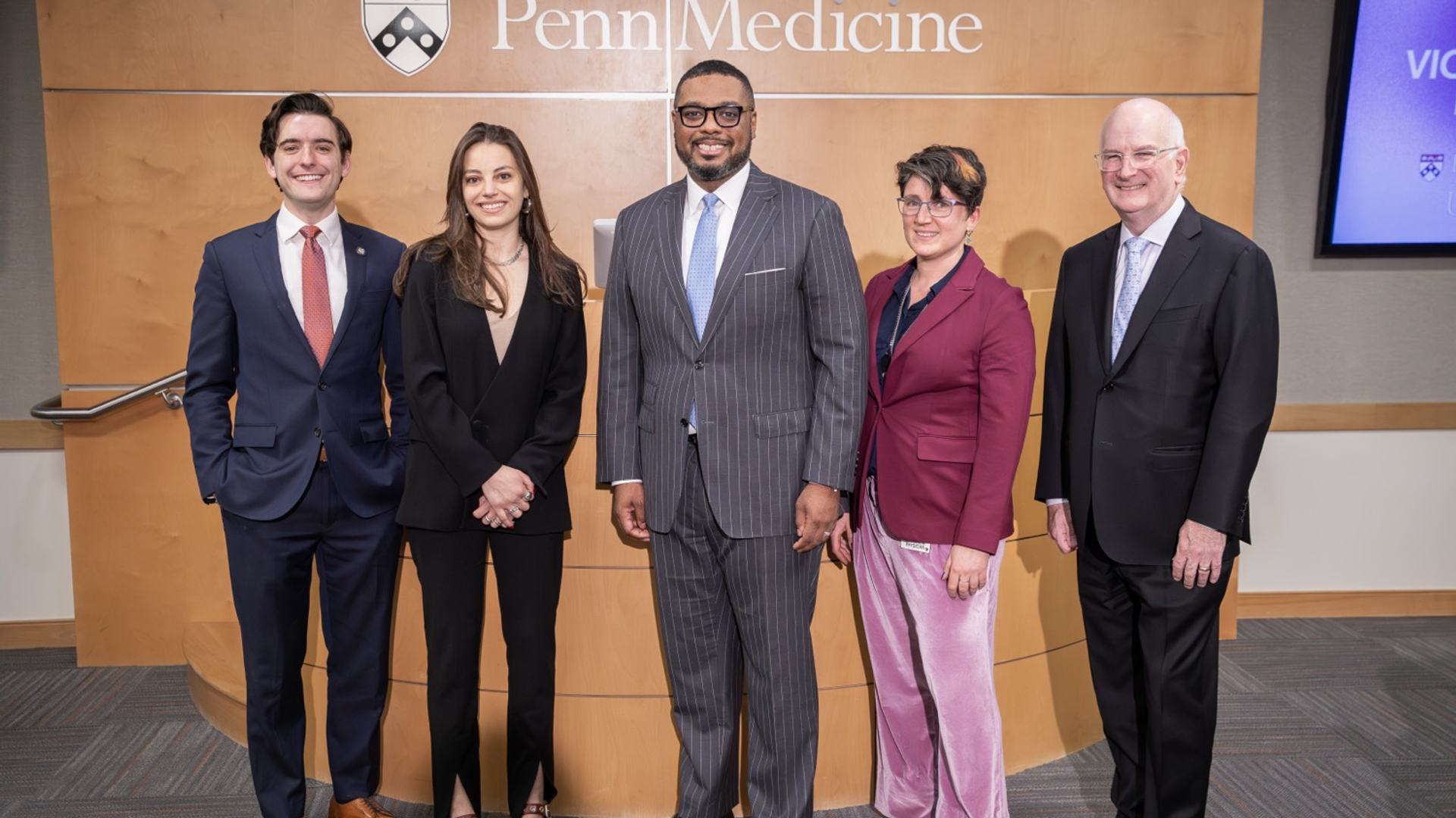 Five adults are standing in a row, dressed in business-casual clothing in front of the Penn Medicine logo.