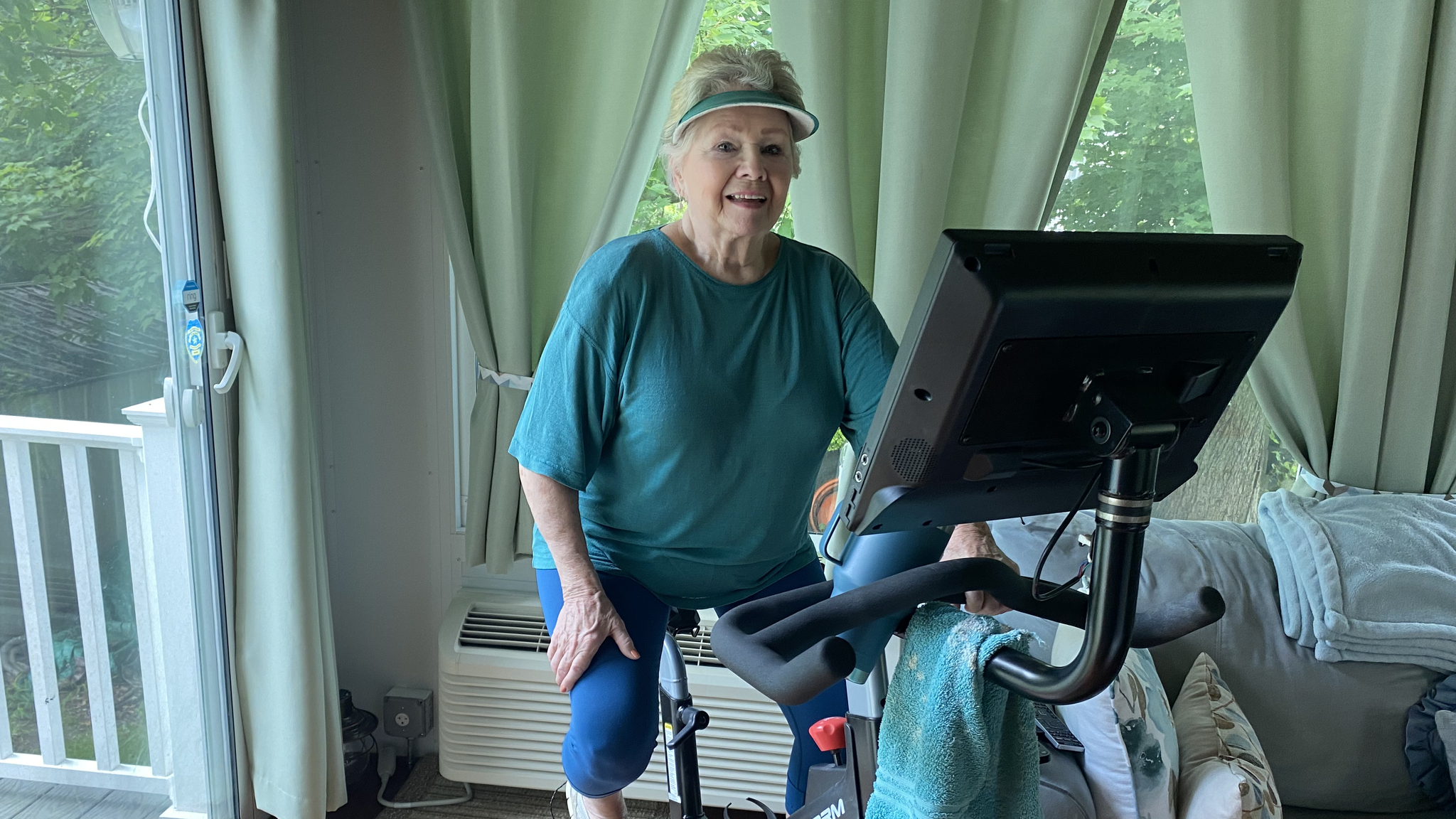 Ellen O'Brien sits on an exercise bike in her home, smiling