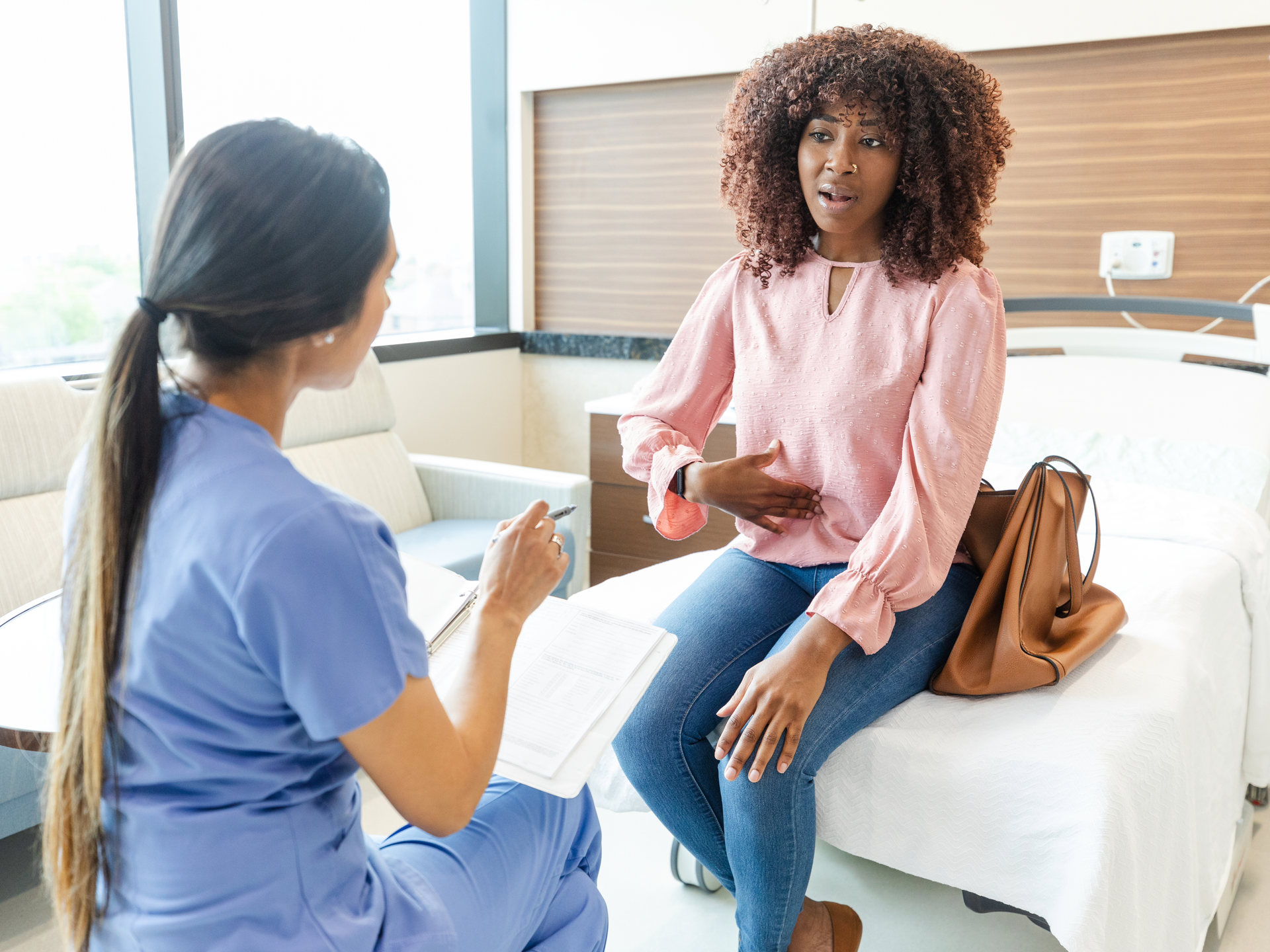 Adult woman gestures toward her abdomen as she describes her abdominal pain to an female healthcare professional