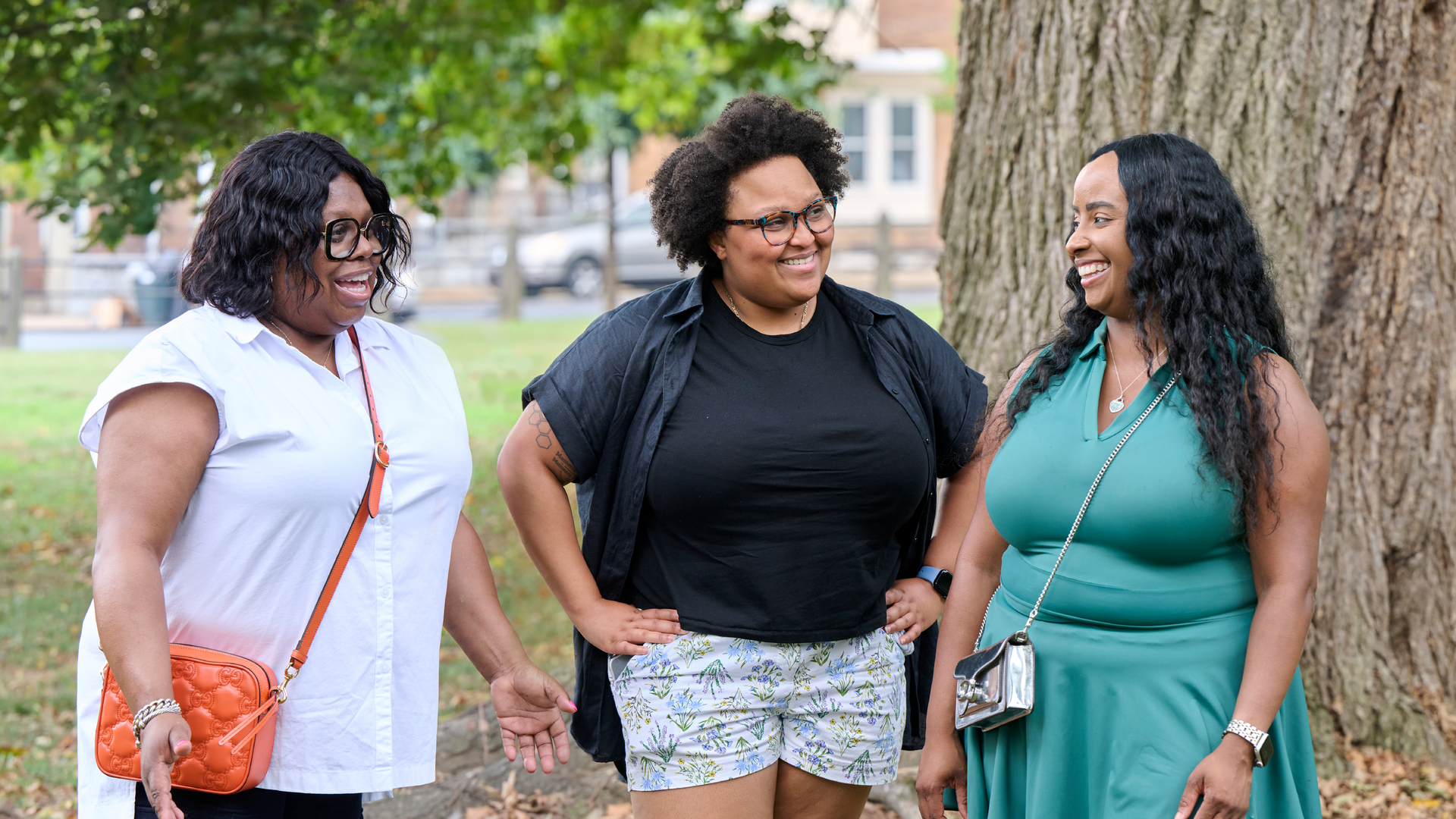 Nicole Thomas, Evan Spencer, and Janaiya Reason stand talking and smiling in a park