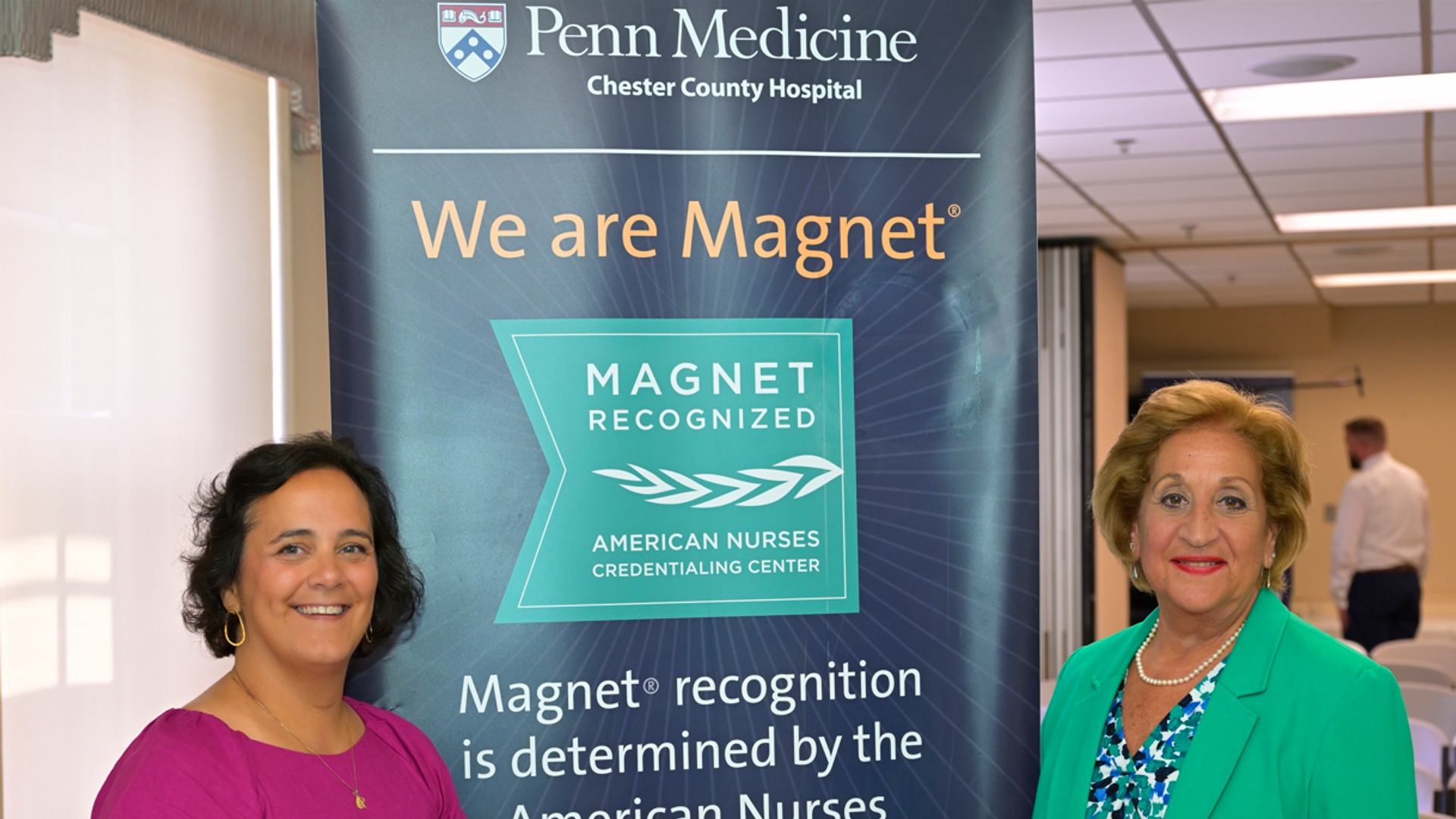 Rosanna Catania-Venuto and Angela Coladonato stand beside a banner that describes Chester County Hospital's Magnet designation with the Magnet logo