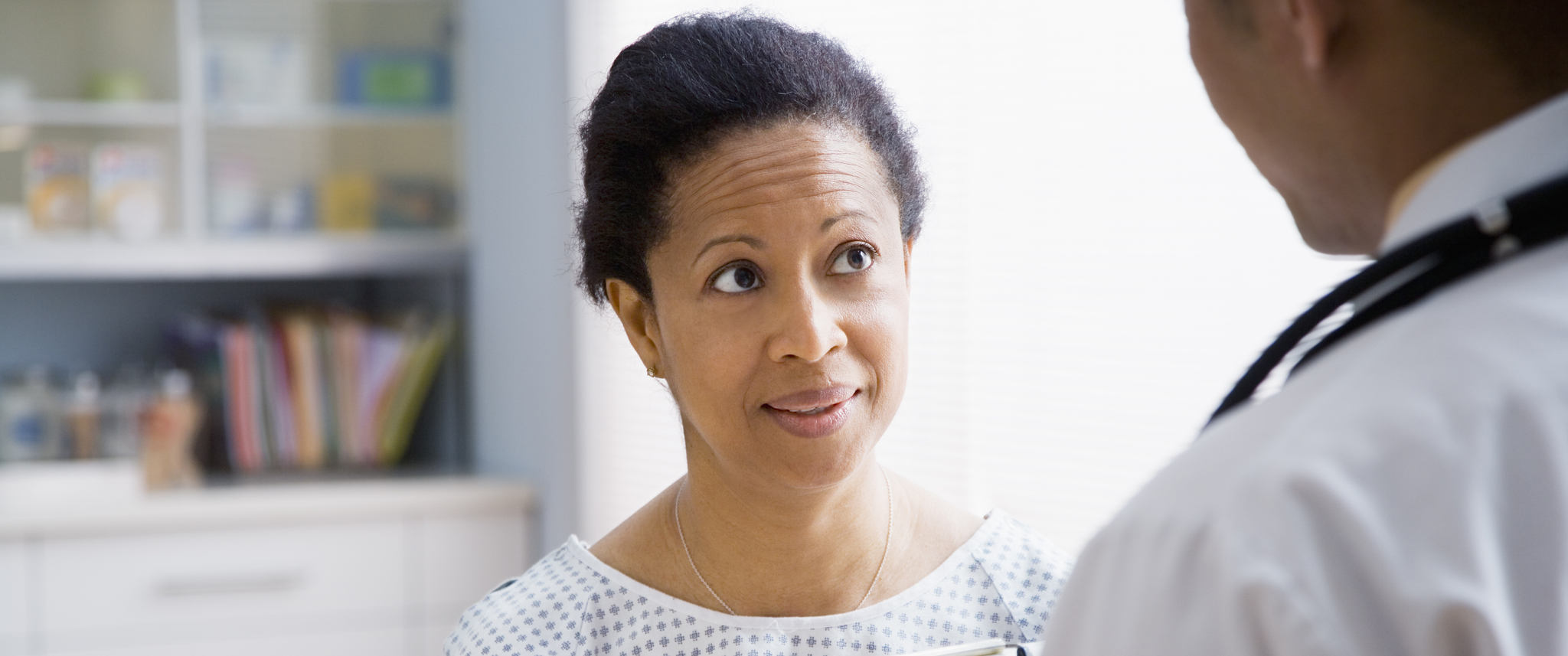 Black woman in hospital gown talking to doctor