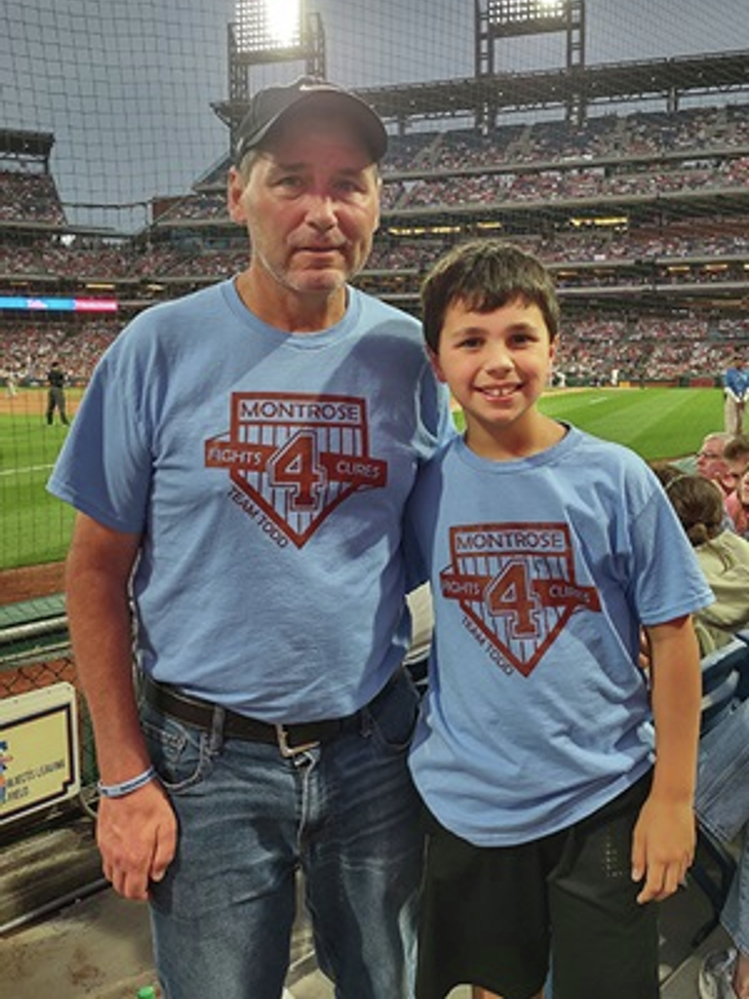Todd Legg standing with his son at a baseball stadium 