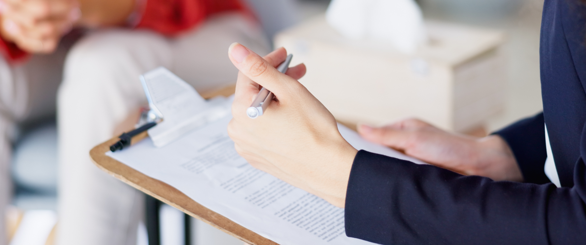 A therapist holding a clipboard and speaking with a patient.